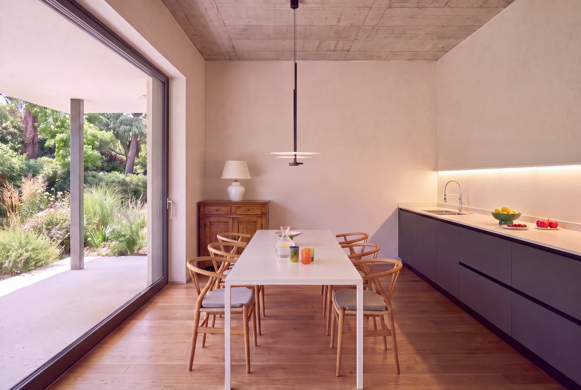 Sala da pranzo con tavolo bianco, sedie in legno chiaro e vetrata sul giardino